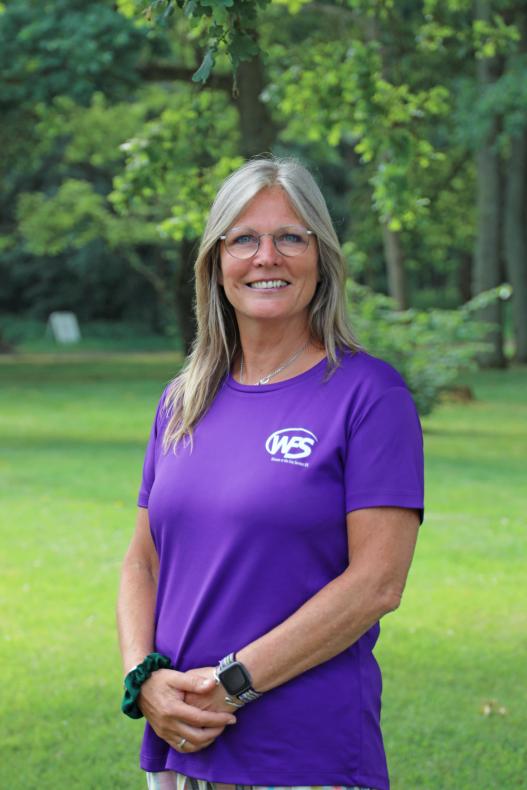 Caroline stood smiling with grass in the background wearing a purple top  