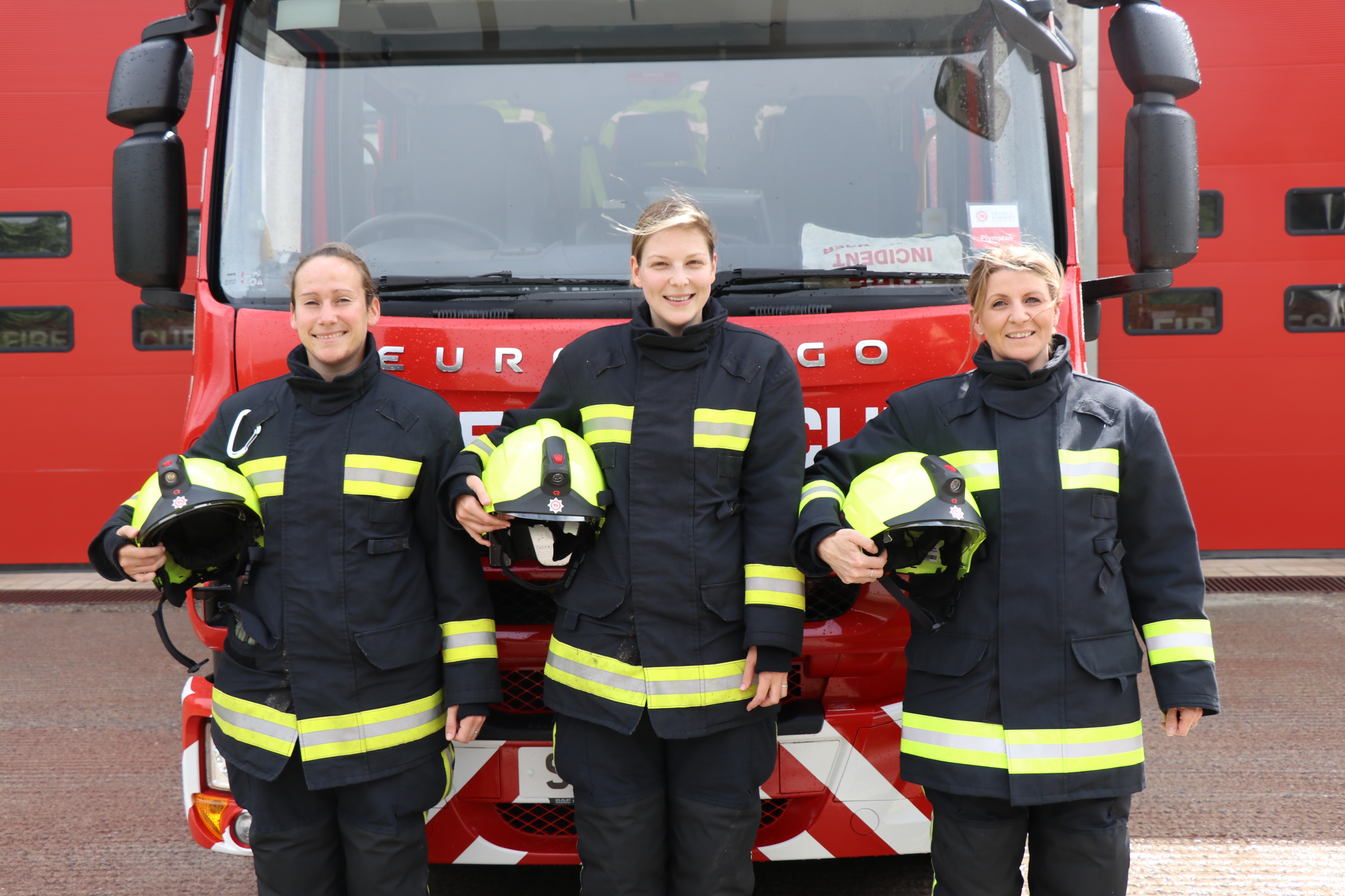 Three female firefighters beside an engine