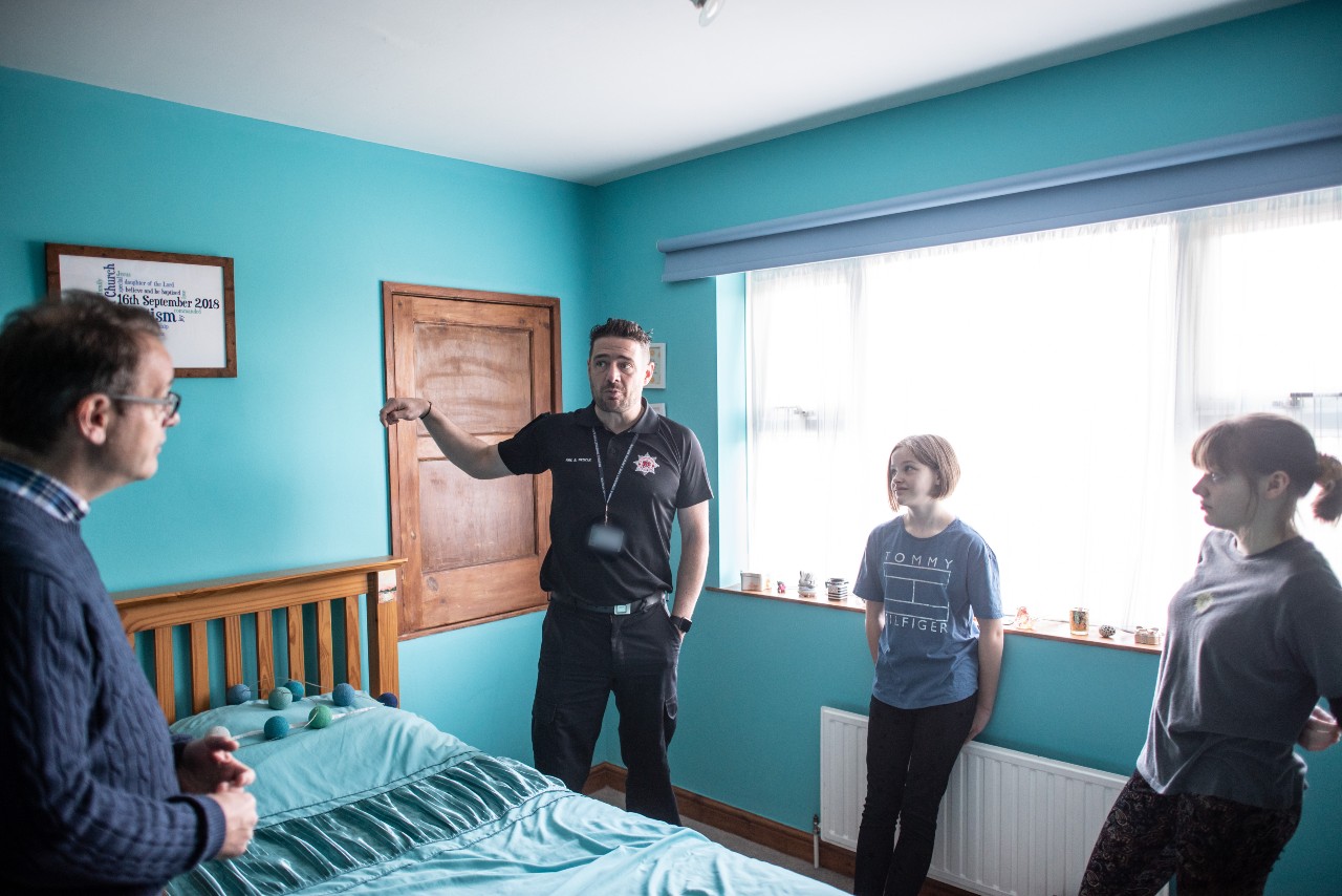 A home safety technician discussing escape routes in a blue bedroom with a dad and his two children.