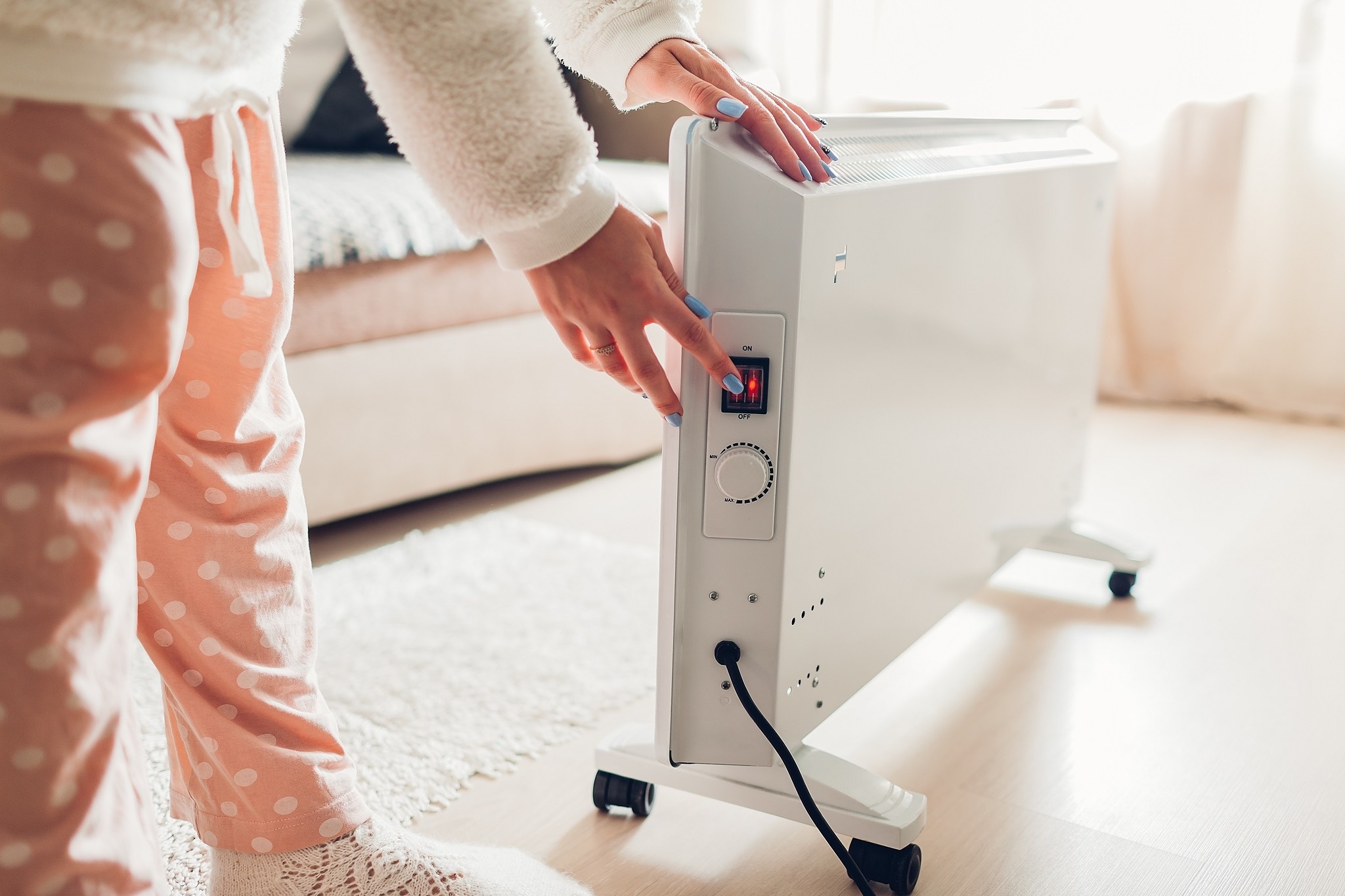 Lady wearing orange pyjamas with white spots leaning down to turn on heater. 