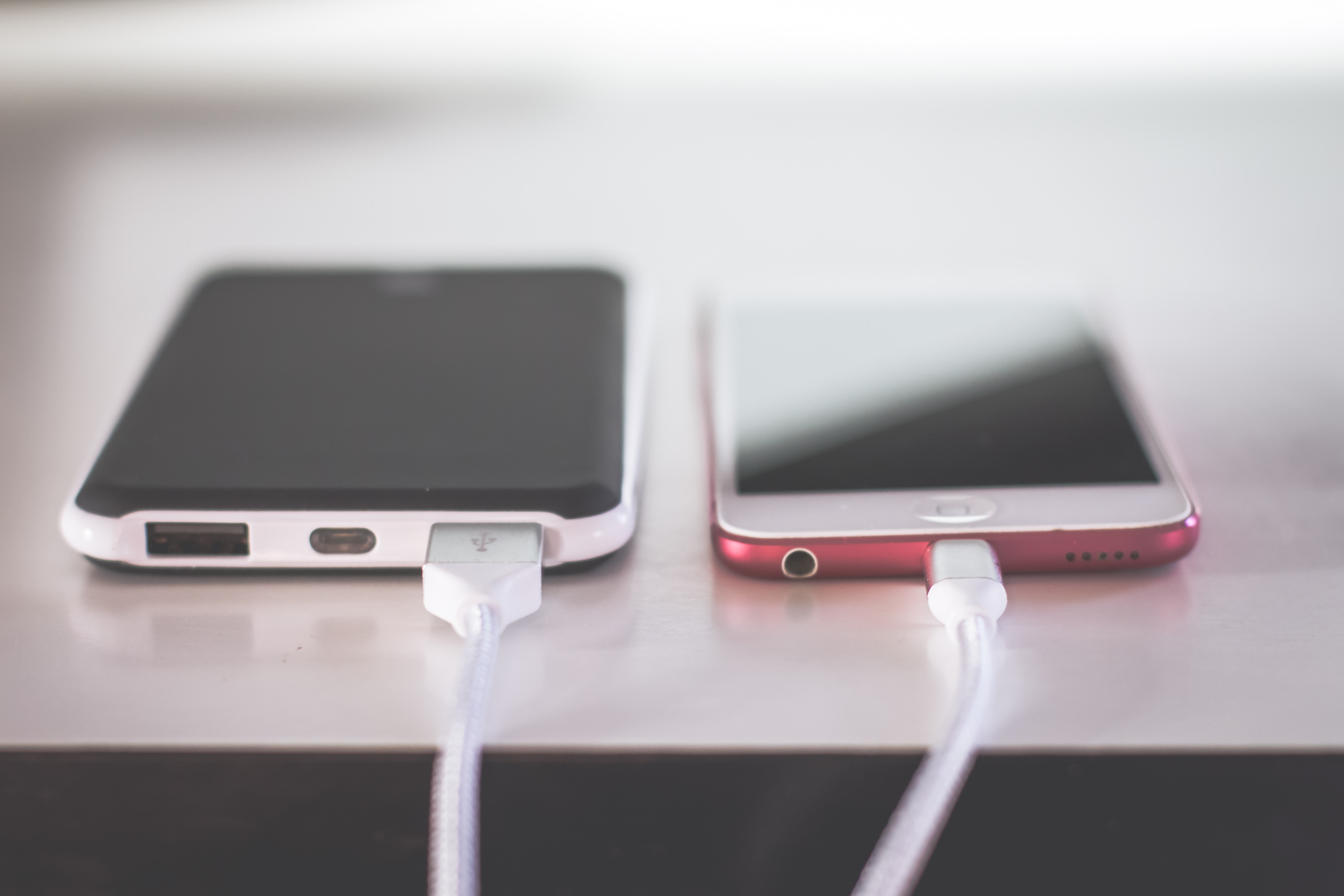 Two phones charging on a hard surface. One is white and one is red.