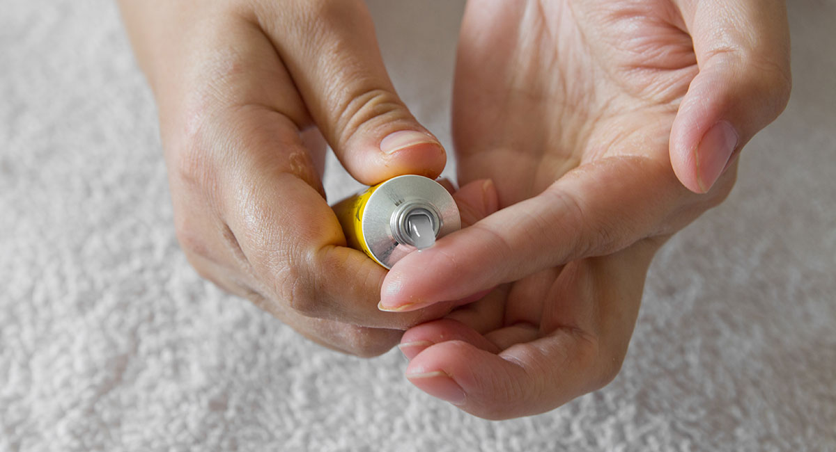 A person squeezes an emollient gel out of a yellow tube onto their hands. 