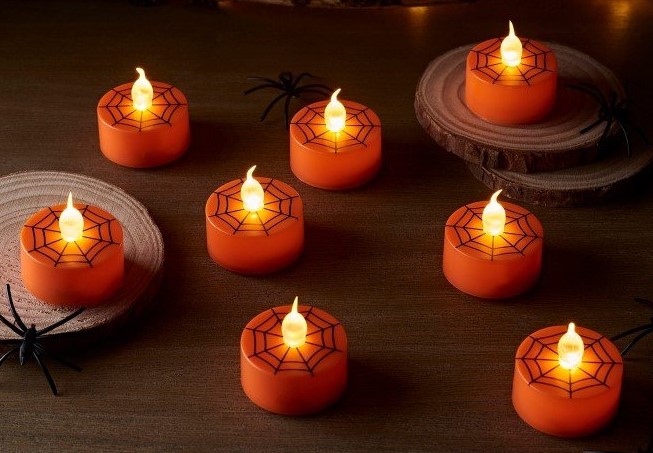 Orange battery-powered tea lights with black spiderwebs. Some fake black spiders are dotted around the table they're on.