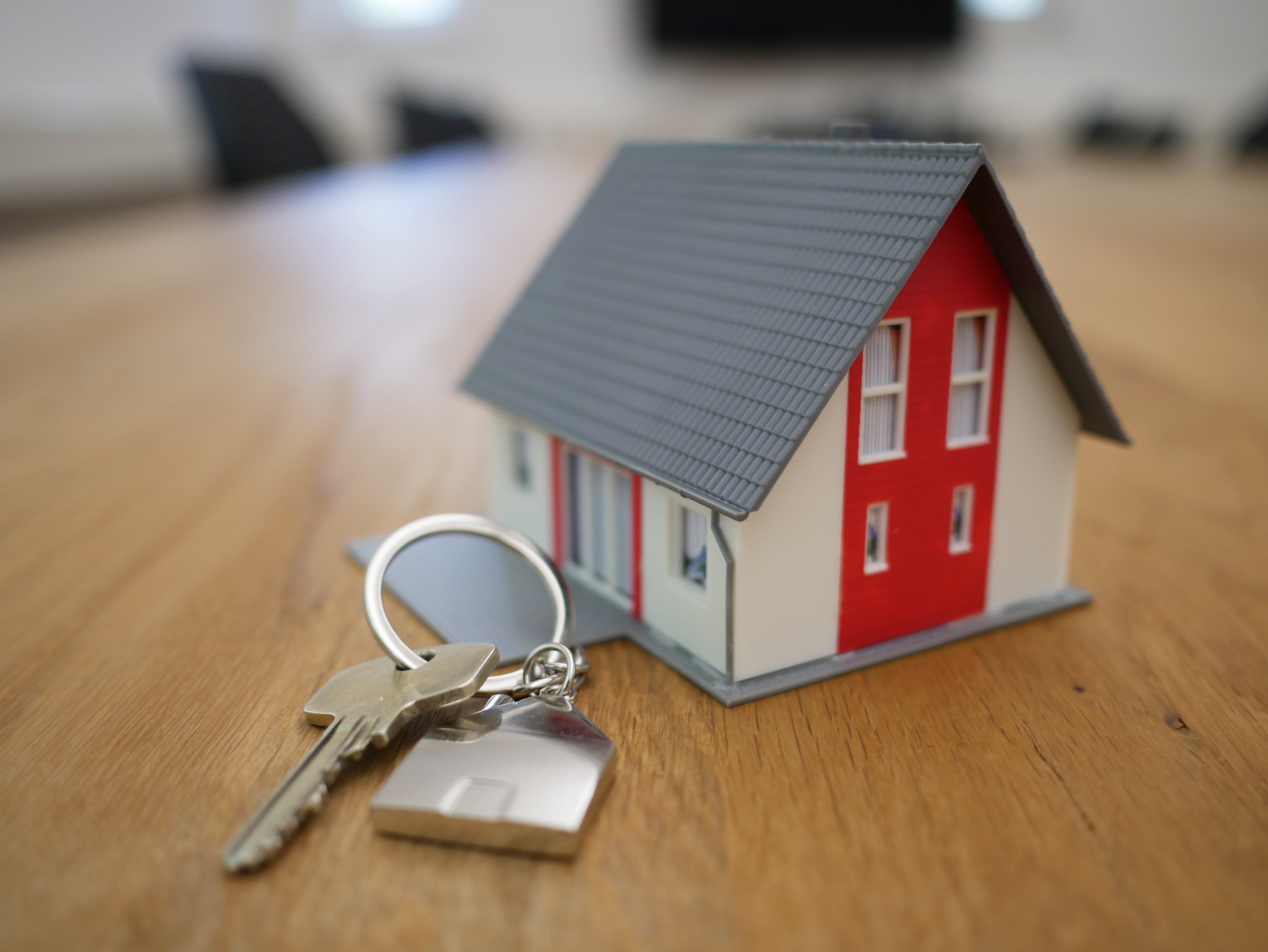 A small wooden house key chain sits on a wooden desk. 