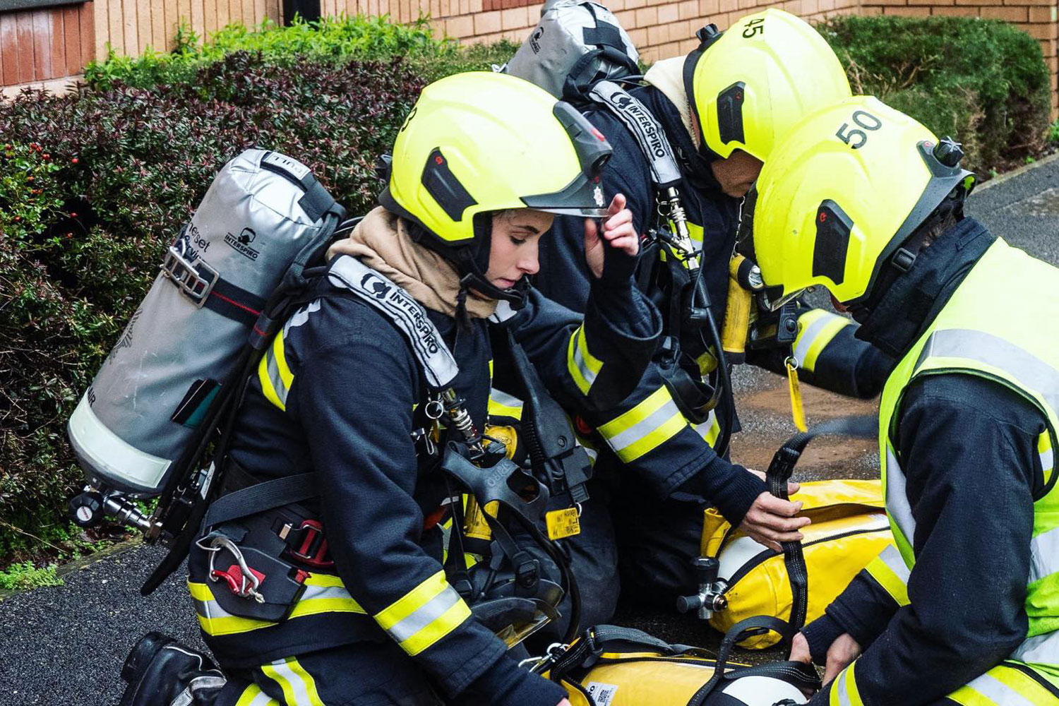 A group of firefighters prepare their breathing apparatus kit for us. The photo is focused on a female firefighter.