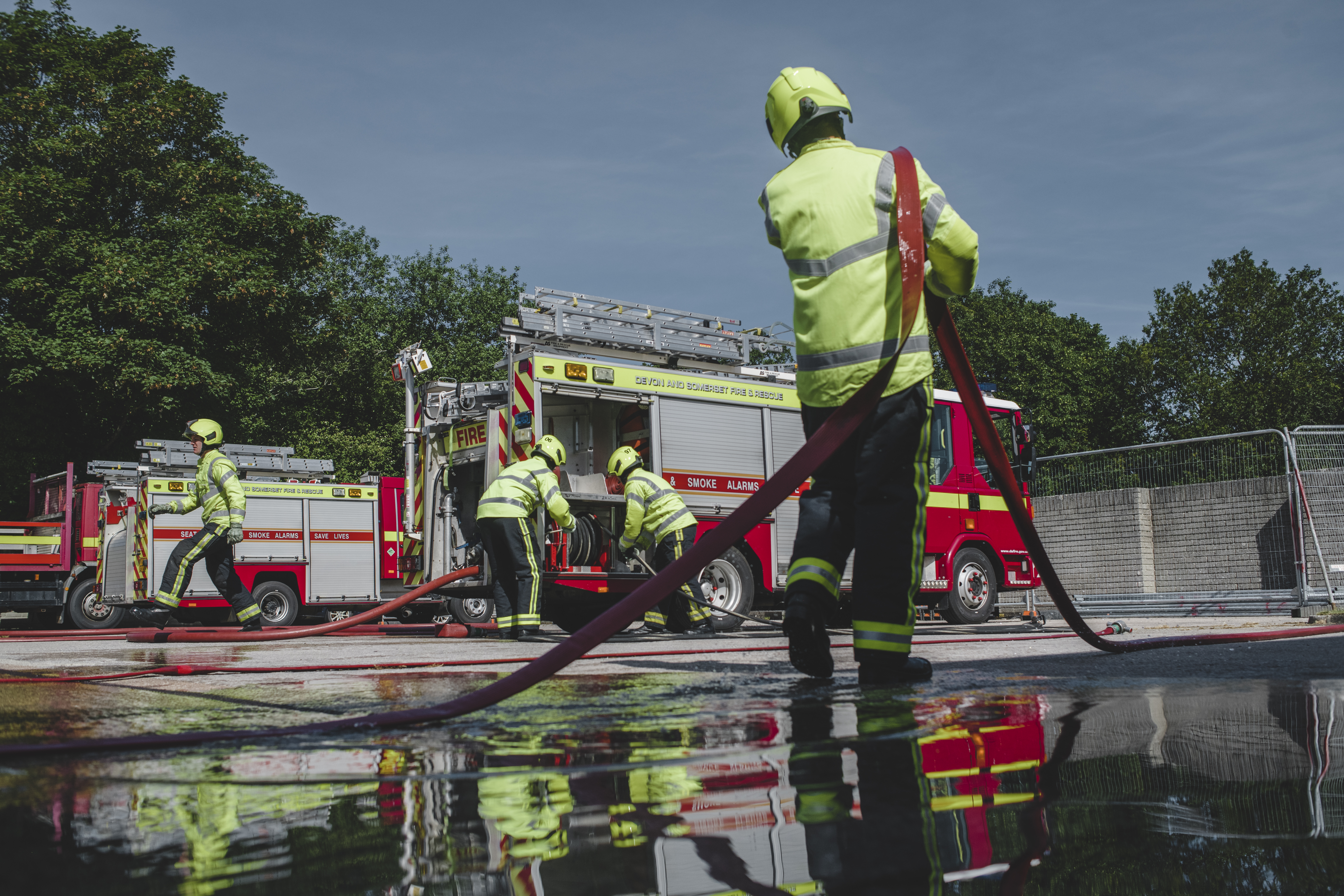 Firefighters in kit, holding red hoses and pulling them out of fire engines.