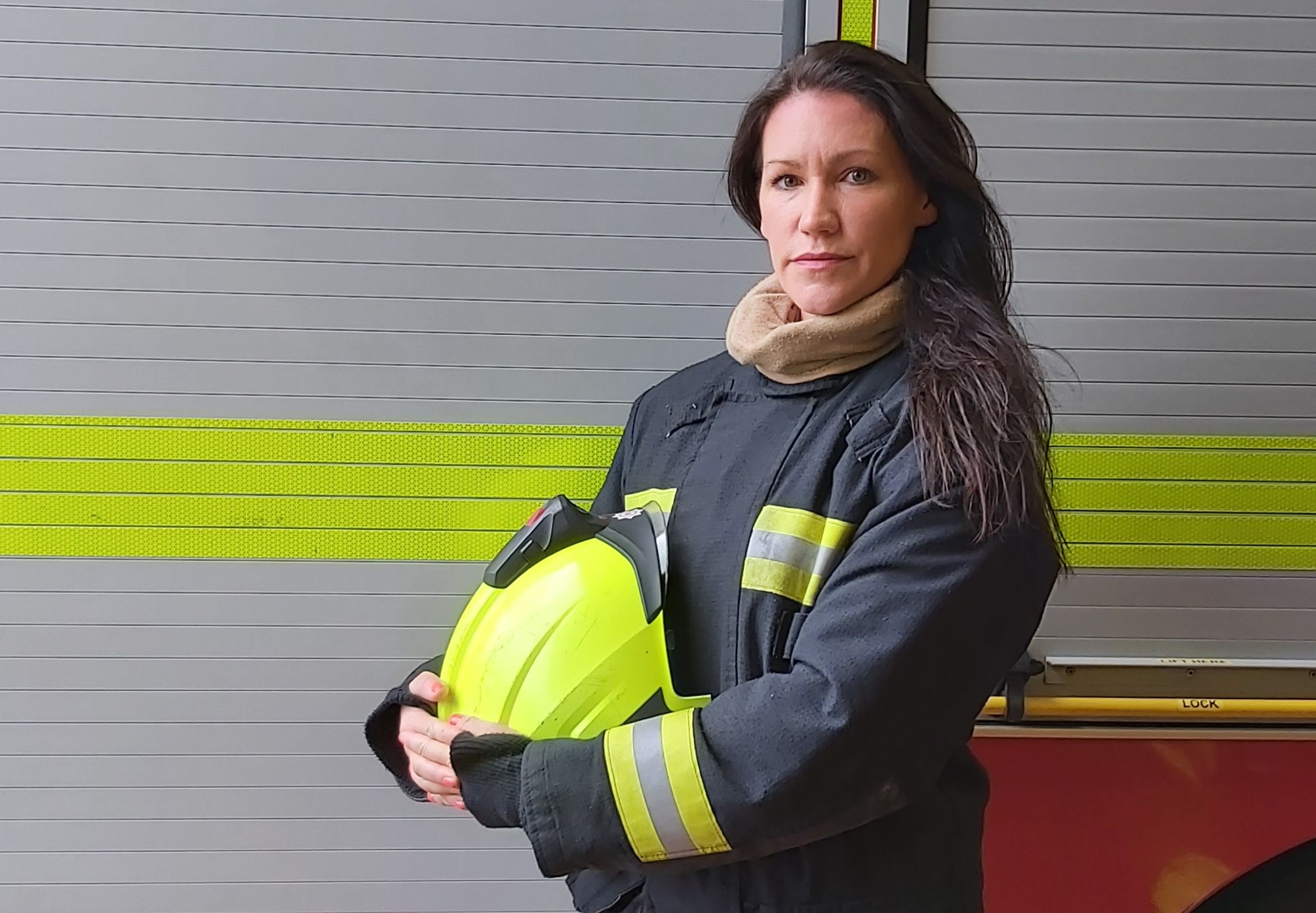 A close-up of firefighter Laura stood in her kit holding her helmet.