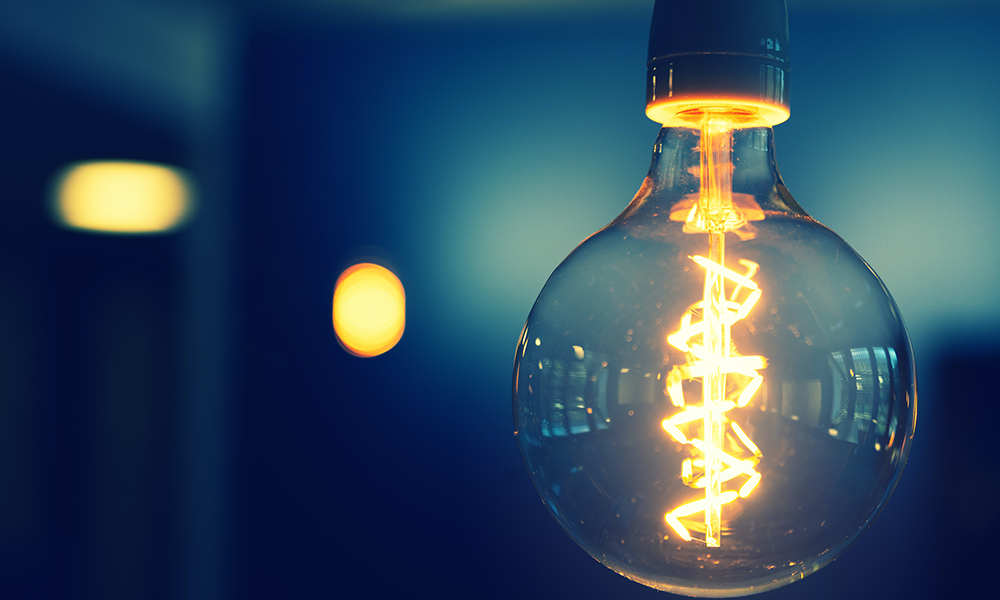 A round light bulb shines up close showing the filament on a blue background. 