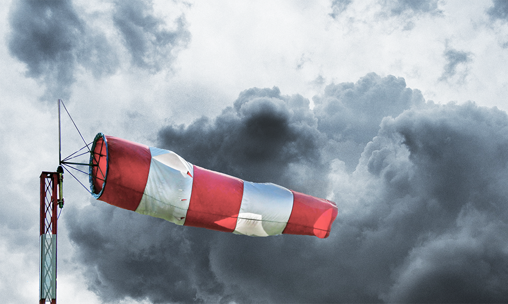 A red and white wind sock blows out in front of a stormy sky