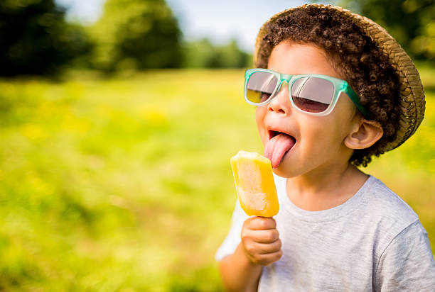 Image of a young boy in a sun hat with glasses licking an ice lolly 