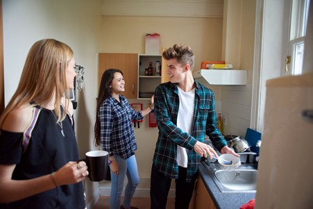 three students are in their kitchen in student halls, one is washing up