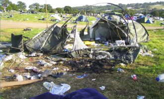A burnt down tent with little material left on it, in a field of other tents, surrounded by rubbish.