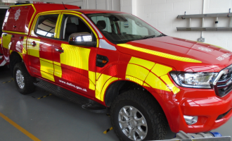 The vehicle has a rather square front, with four doors to get in to the seats. The back storage space is slightly higher than the front, with the Service logo on the side. The design is neon yellow and red blocks along the side, with the rest of the vehicle the usual red. 