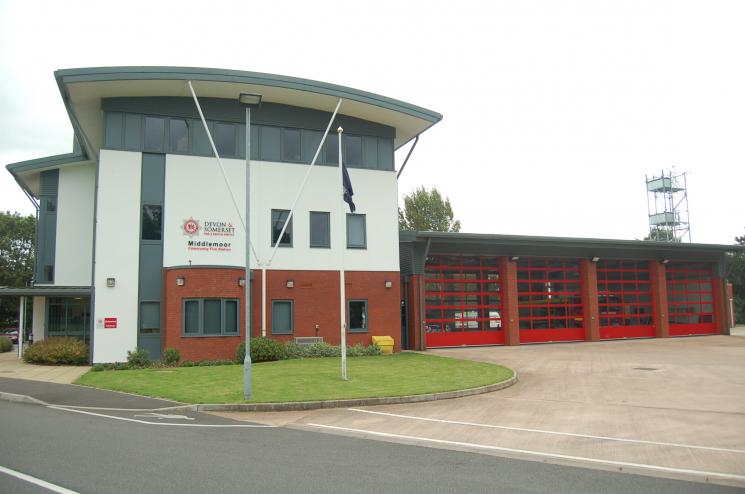 A photo of Middlemoor Fire Station, which has a three floor white, grey and brick building next to four garages with doors and windows.