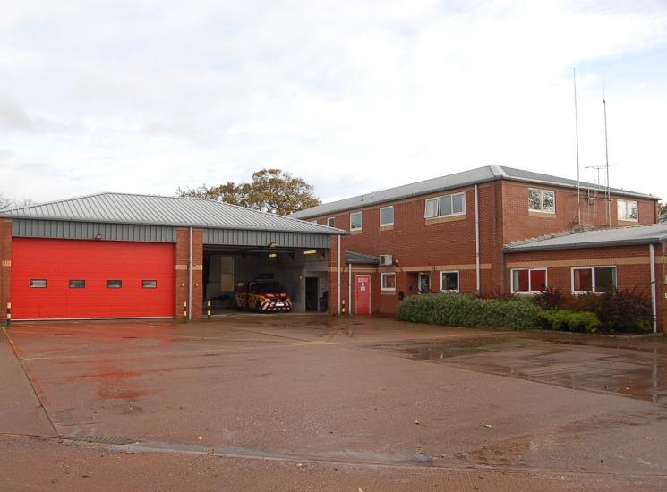 A photo of Exmouth Fire Station's two garages, with one open showing a van inside, next to a brick building.