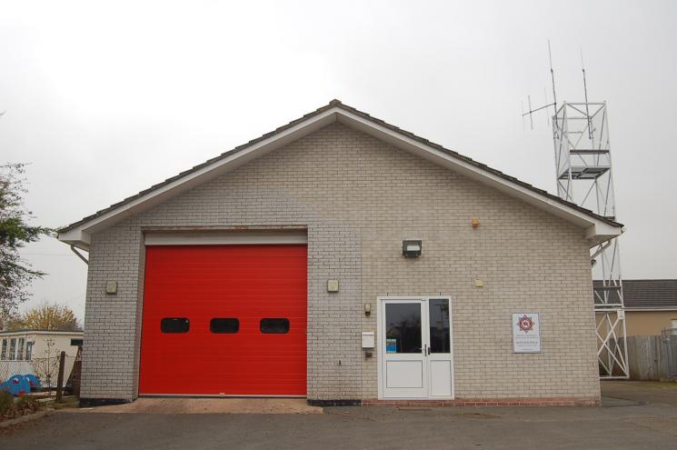 A photo of Witheridge Fire Station, which is a block brick building with the red garage included.