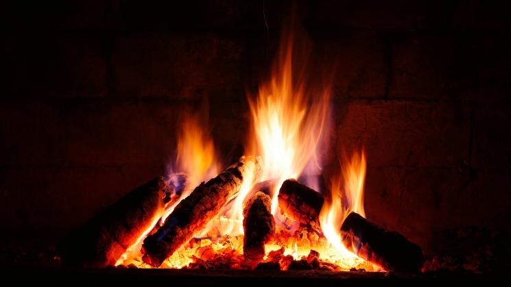 A close-up photo of a fireplace, with piled logs and orange, yellow flames.