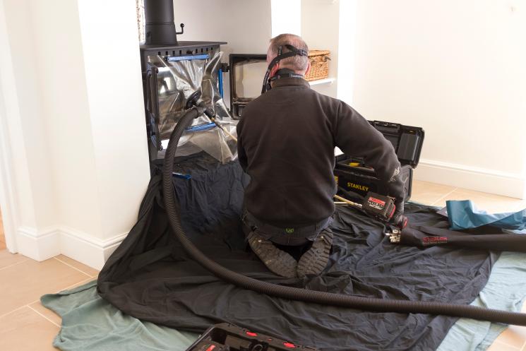 A chimney sweep using equipment inside of a home in full gear.