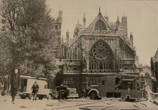 A photo of fire engines in front of the Exeter Cathedral. There are hoses all across the ground and a few firefighters can be seen walking around.