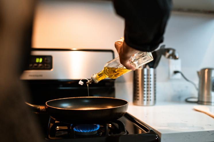 Someone pouring oil from a glass bottle into a pan on the hob.