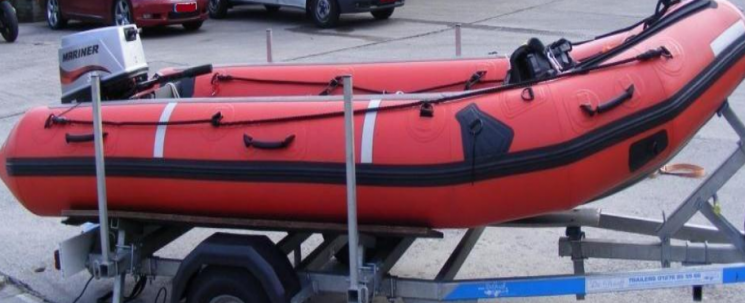 A red inflatable raft with a small silver engine on the back. It's got a black line around the middle and is on a silver trailer.