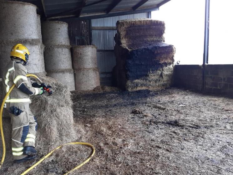 smouldering hay bales in a barn being watched by firefighter