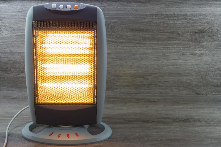 A halogen heater on the floor. It has yellow lights behind a grated cover, and is light and dark grey around the outside. There are a few buttons on the top.