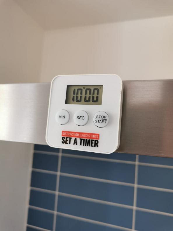 a white digital cooking timer attached to a metal extactor fan in a kitchen. The timer reads 'distraction causes fires - set a timer'