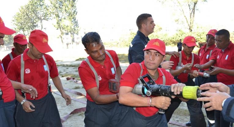 Firefighters being trained in Nepal. They're wearing their firefighter kit, which is all red, and a couple of them are holding hoses whilst the others nearby observe. One of our firefighters is stood amongst them, and one is just off camera helping.