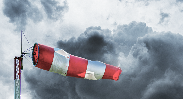 A red and white wind sock blows out in front of a stormy sky